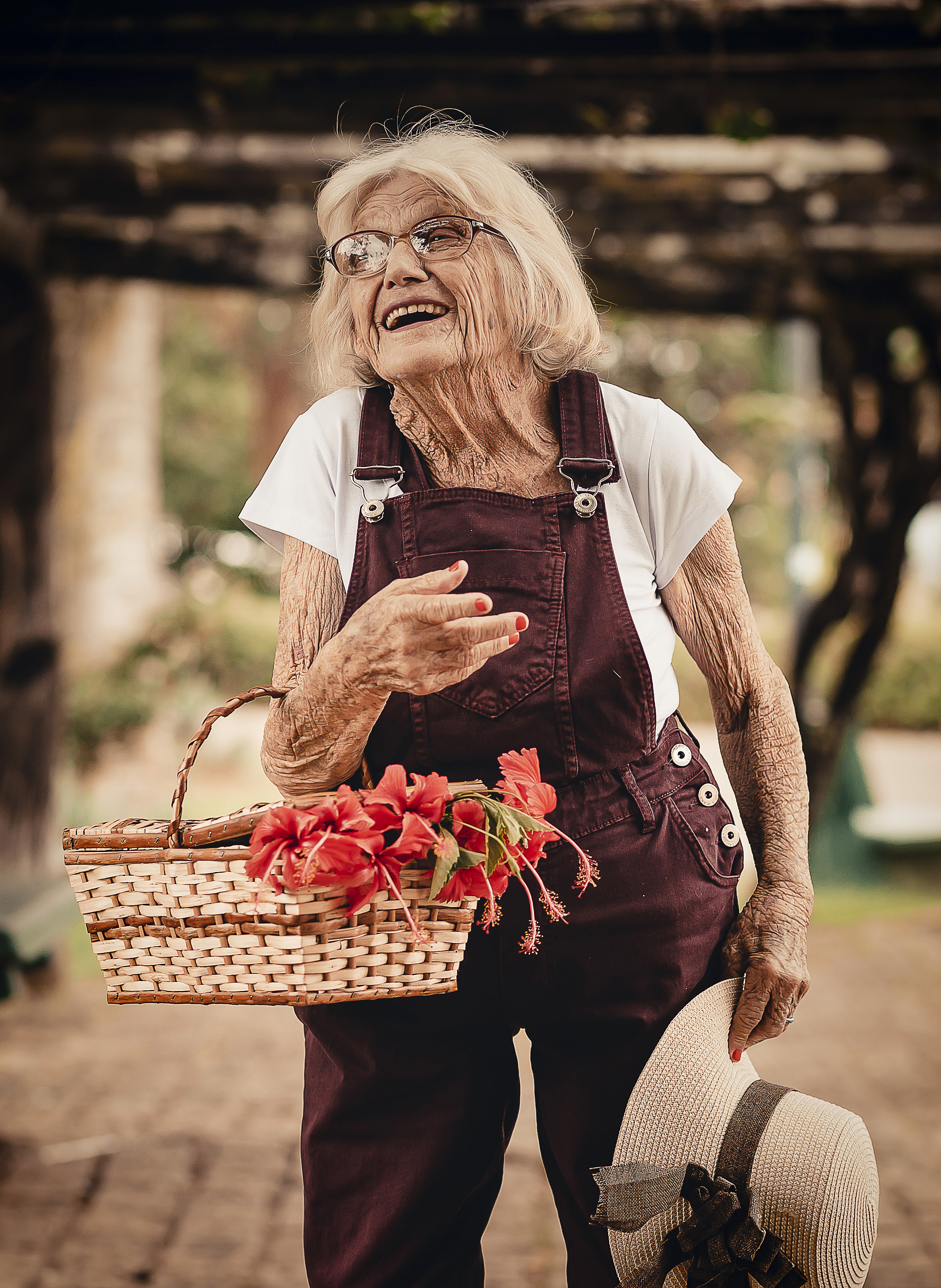 Overall wearing Lola smiles holding basket of red hibiscus flowers