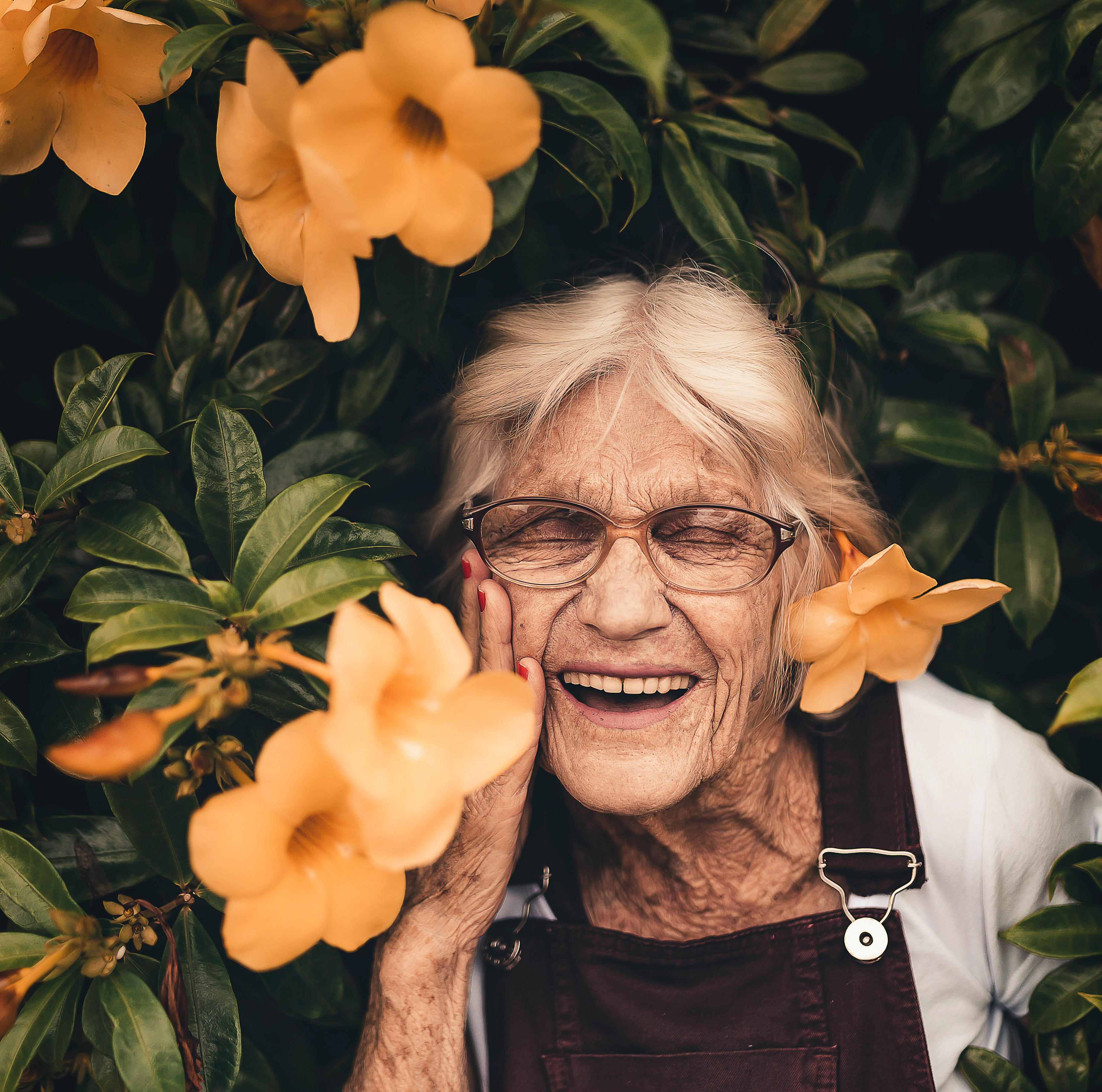 Lola Flora smiling eyes closed wearing glasses and overalls among yellow flowers